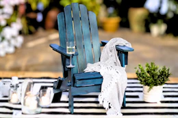 Lifestyle image of a navy wood Adirondack chair in an outdoor setting on a striped rug