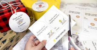 Someone cutting out some KCL free printable gift tags next to some wrapped presents with gift tags on them