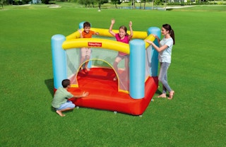 stock photo of kids jumping in fisher-price bounce house on big grassy area