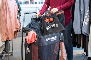 A person putting Nike and Under Armour activewear into a Kohl's shopping cart.