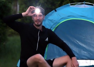 a person wearing a flashlight headlamp in front of a tent