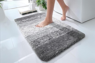 Two feet getting out of a bathtub and stepping on a multi-tone grey plush rug