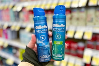 hand holding two cans of spray deodorant in store aisle in front of shelves with sales tags