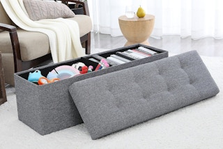 An opened gray storage ottoman from QVC with various items stored inside. 