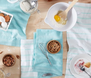 four blue and white kitchen towels on a counter with cooking supplies