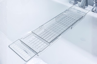 Lifestyle image of the Atomi Expandable Clear Acrylic Caddy Bathtub Tray over a bathtub