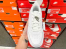 An Airforce one Nike shoe held out in front of multiple Nike boxes sitting on a shelf.