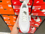 An Airforce one Nike shoe held out in front of multiple Nike boxes sitting on a shelf.