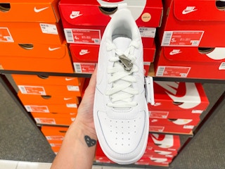 An Airforce one Nike shoe held out in front of multiple Nike boxes sitting on a shelf.