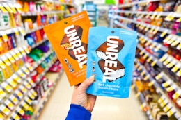 person holding 2 bags of unreal chocolate bars in an aisle