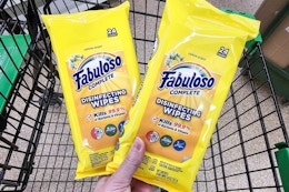 person holding 2 packs of fabuloso cleaning wipes over a cart