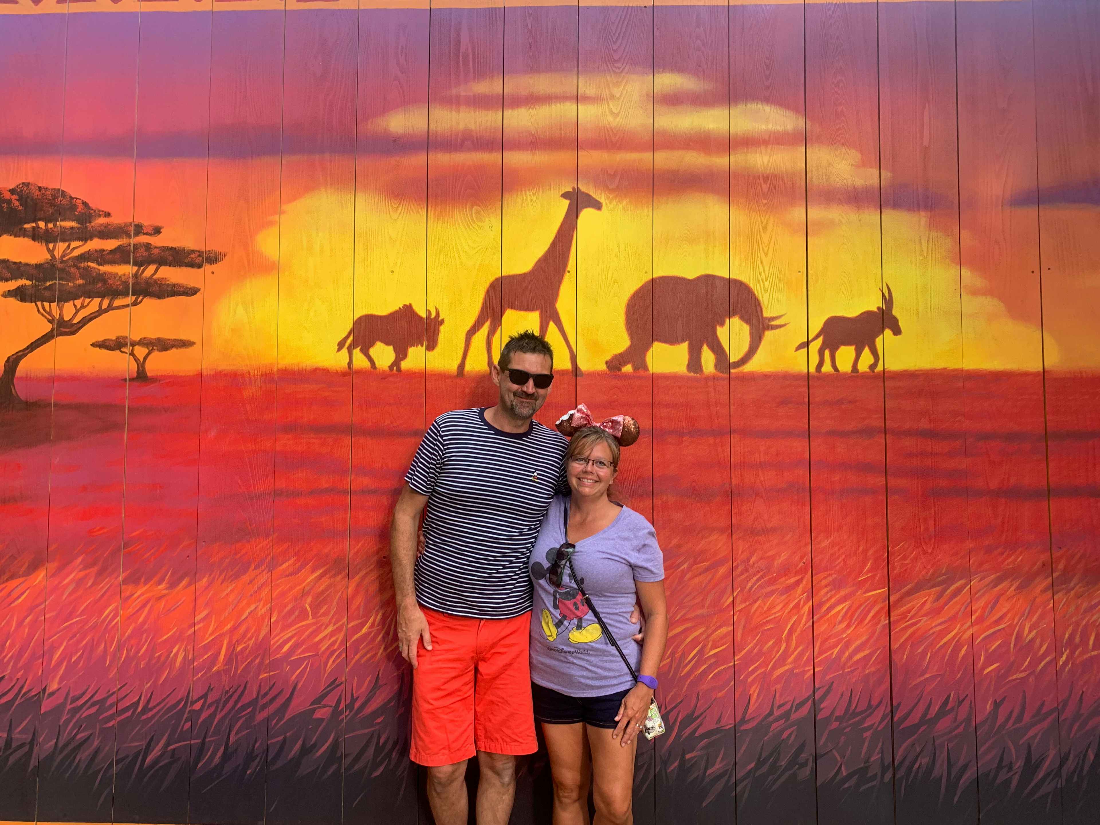 two people standing in front of a lion king backdrop at disney world