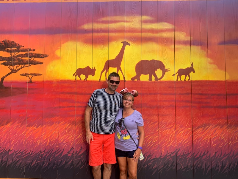 two people standing in front of a lion king backdrop at disney world