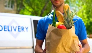 Person carrying a paper bag of groceries with a delivery truck in the background