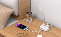 a nightstand with a powerstrip charging devices and glasses