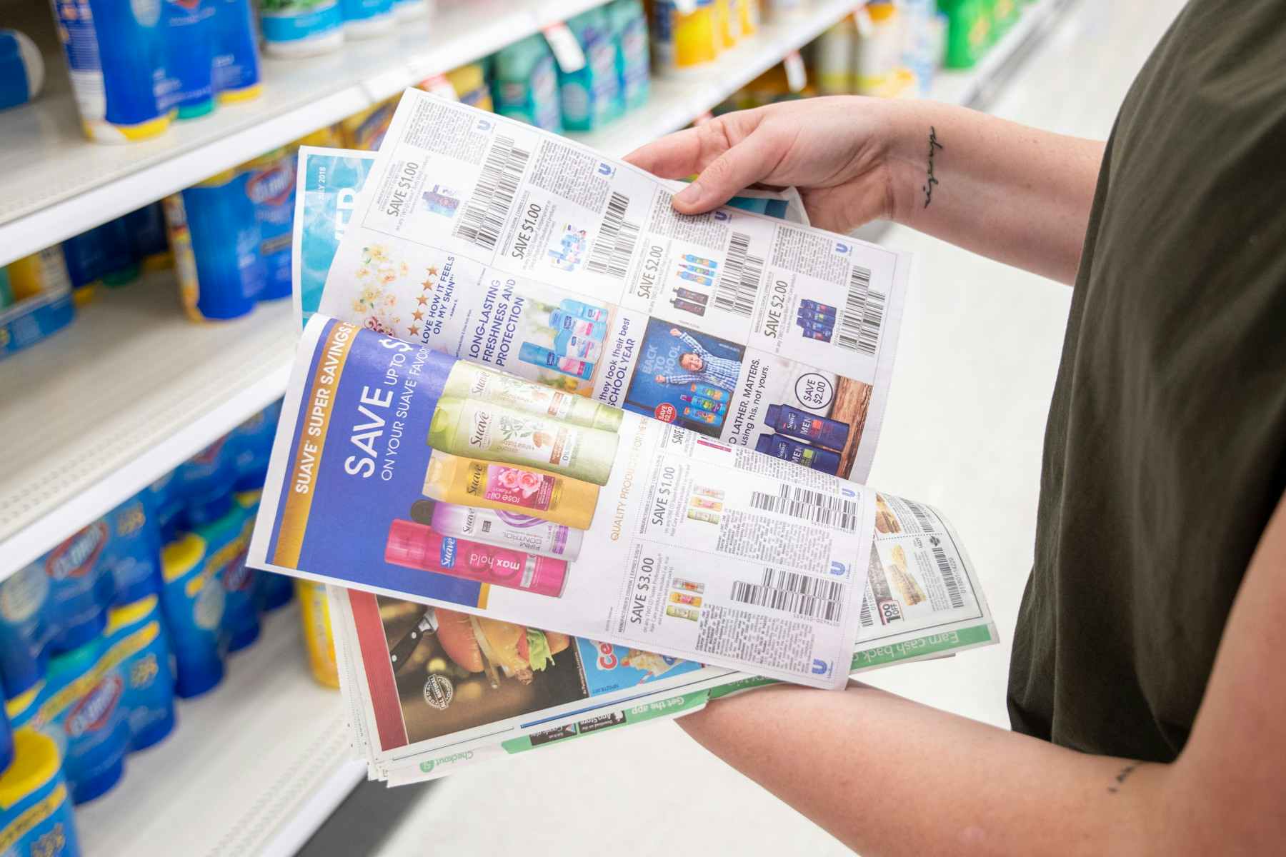 A person flipping through newspaper coupons while standing in a store aisle.