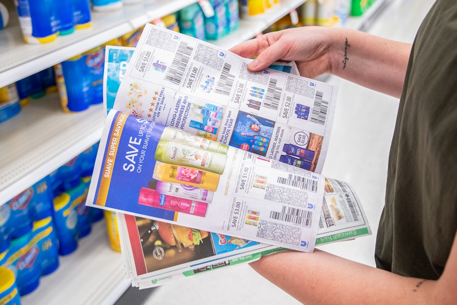 A person flipping through newspaper coupons while standing in a store aisle.
