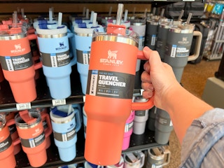 A person holding a grapefruit colored Stanley quencher cup.