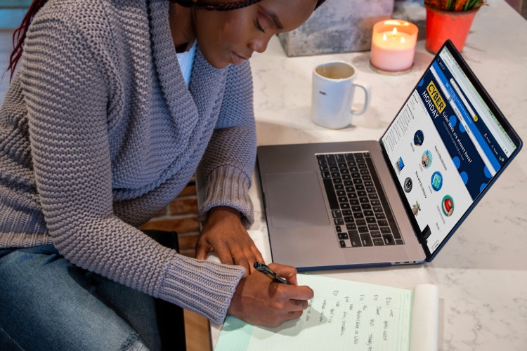 A woman writing down on a notepad next to a laptop with Walmart Cyber Monday webpage displayed.