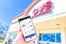 hand holding a smartphone in front of a CVS store displaying KCL coupons