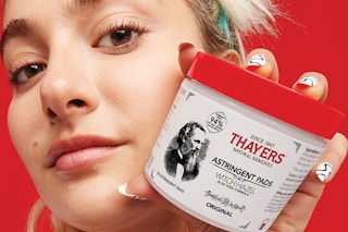 a person holding a white and red container of acne pads