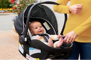 Woman holding a Graco Car Seat with an infant in it.