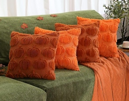 four rust and orange pumpkin-designed pillows on a green sofa