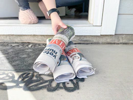 a person grabbing a newspaper from porch