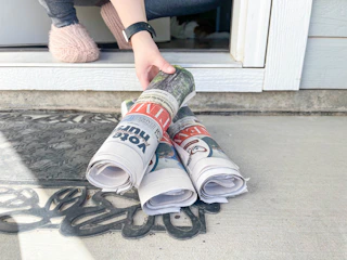 a person grabbing a newspaper from porch