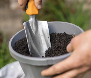 a hand shovel digging in a pot of soil