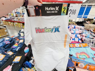 hand holding a 2 pack of hurley kids tshirts, front shirt is white with hurley written in rainbow