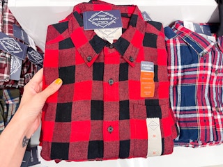 A hand holding a men's flannel shirt sitting out in front of other flannel shirts.