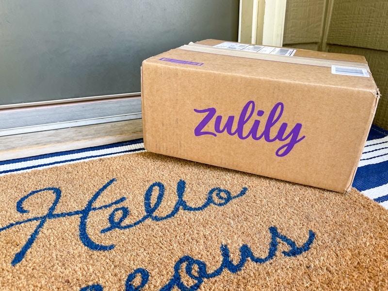 A Zulily box sitting on a front porch in front of someone's front door.