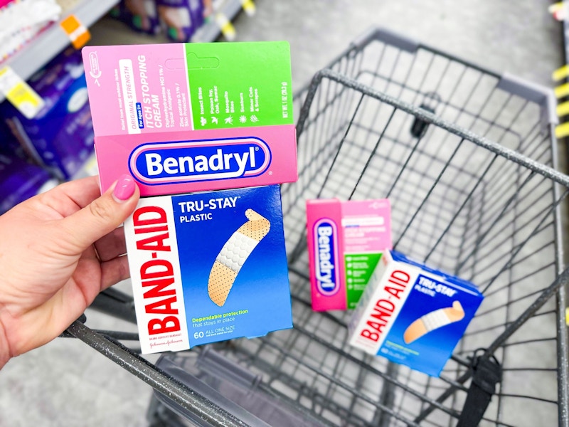 person holding a package of bandaids and benadryl cream over a cart