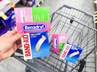 person holding a package of bandaids and benadryl cream over a cart