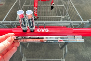 hand holding lip and eye liner with lip stick balancing on shopping cart handle