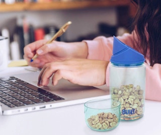 A little girl on a computer with a snack container next to her
