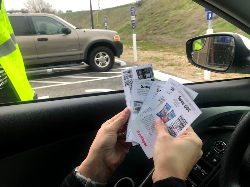 A person in a car holding coupons to hand to a clerk at grocery pickup.