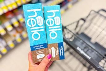 person holding 2 hello toothpastes over a walgreens cart