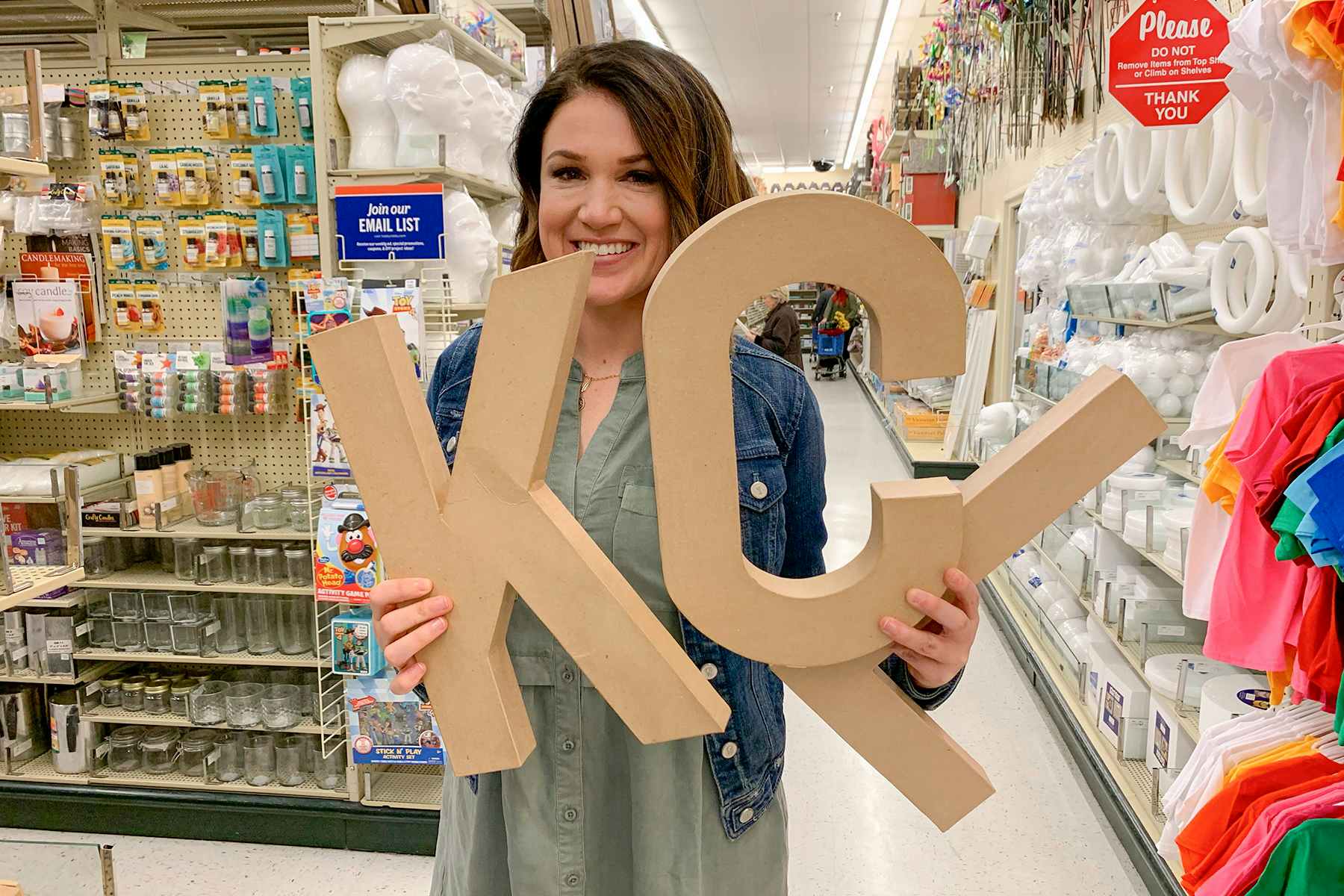 One of the owners of thekrazycouponlady.com, holding up large cardboard letters that read "KCL".