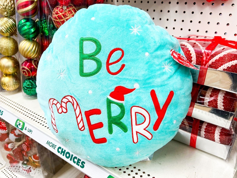 blue pillow that says be merry on a shelf