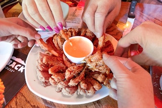 People reaching to take a piece of a bloomin onion appetizer at Outback Steakhouse