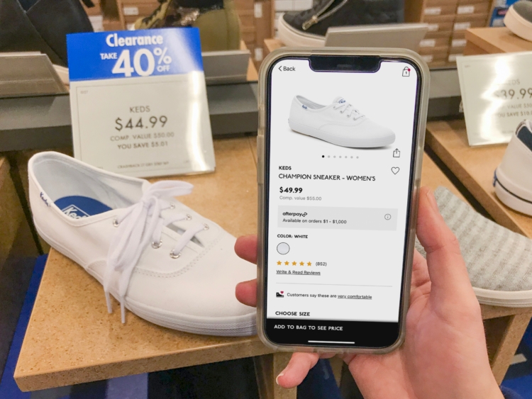 A white shoe on display with blue sales tag reading "40% off". A cell phone is held with the same shoe on the DSW app, with a regular price.
