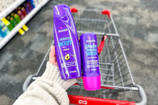 hand holding two aussie hair products over a cvs shopping cart