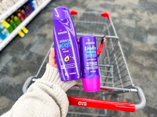 hand holding two bottles of aussie hair care next to a cvs shopping cart