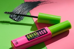 a mascara tube and wand on a pink and green background