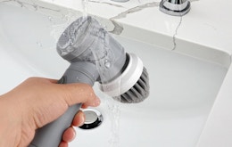 a hand holding a spin scrubber under a faucet