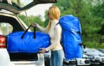 a woman carrying two big blue moving bags to her car's truck