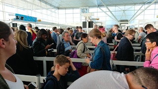 Travelers standing in long lines inside an airport.