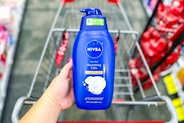 person holding a bottle of nivea body wash over a cvs cart